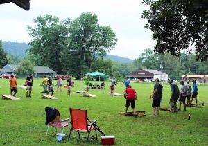 cornhole tournament held in a park with competitors mid-toss, cornhole boards